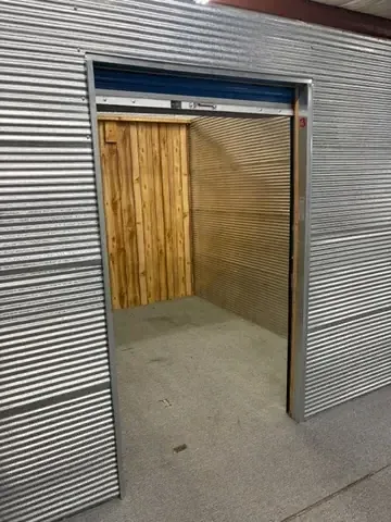 Inside an empty indoor storage unit with corrugated steel walls, wood-paneled back wall and an open roll-up door at American Mini Storage in Staunton, VA